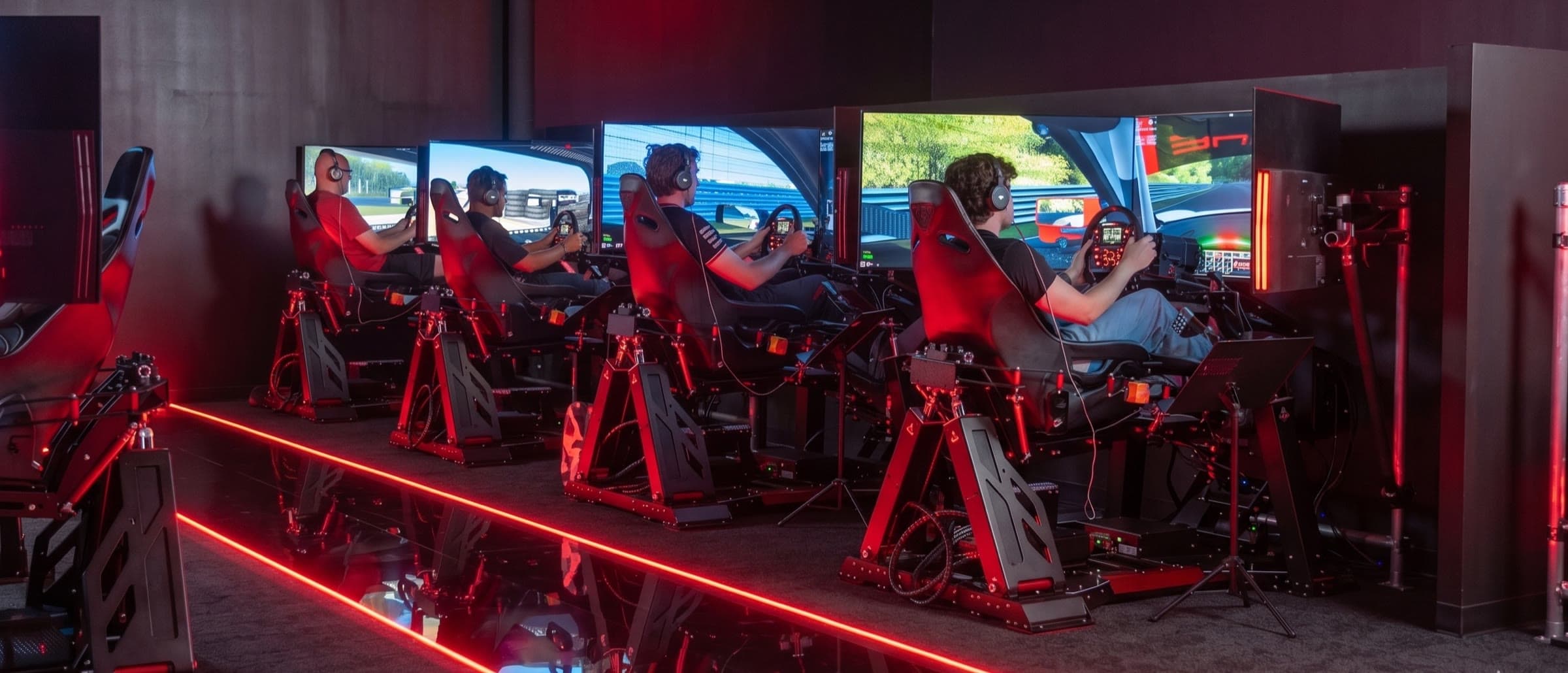 Four drivers racing side by side on full-motion sims under red light