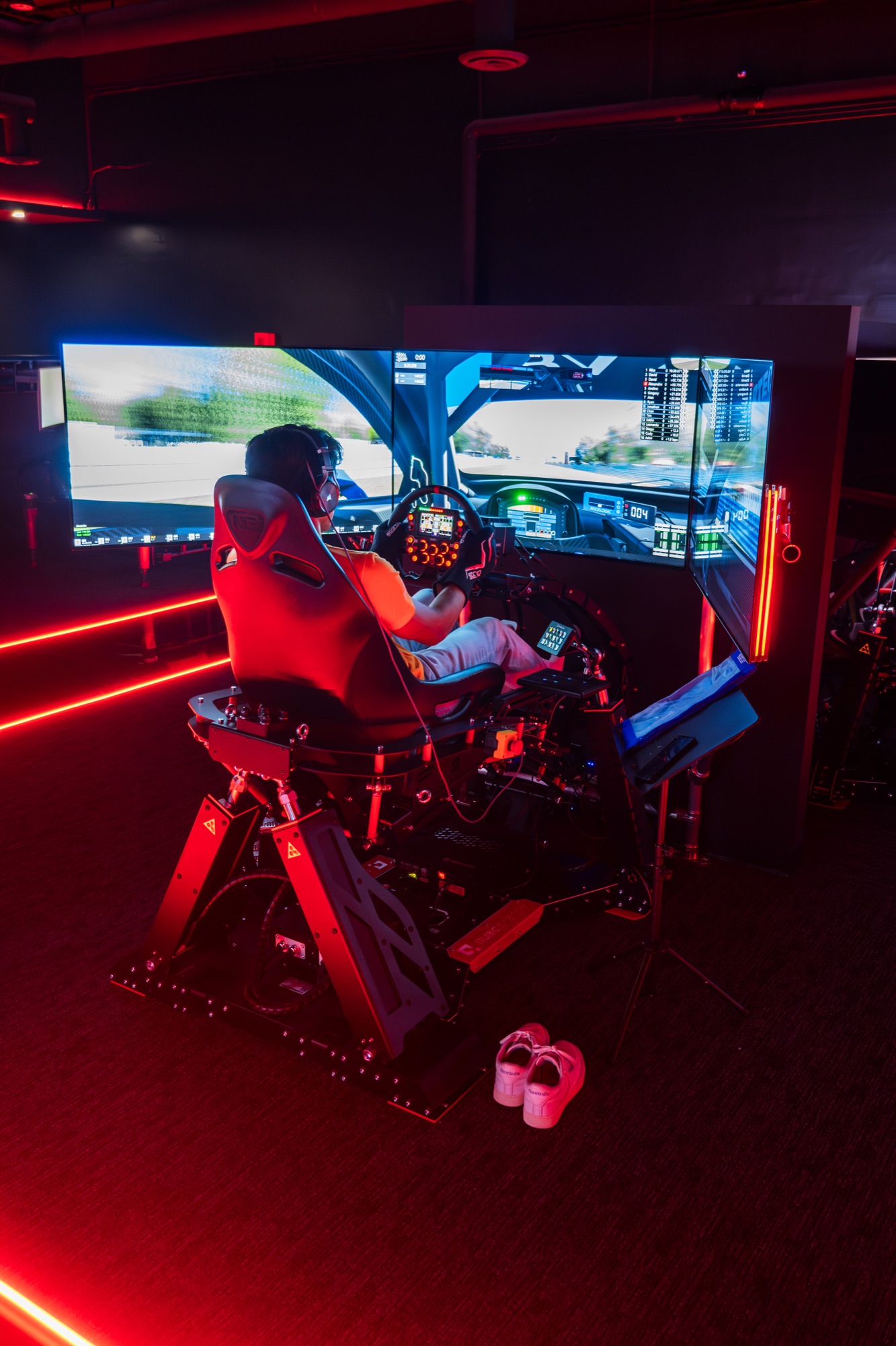 Driver from behind at a World of Racing rig, mid-session under the neon-track ceiling