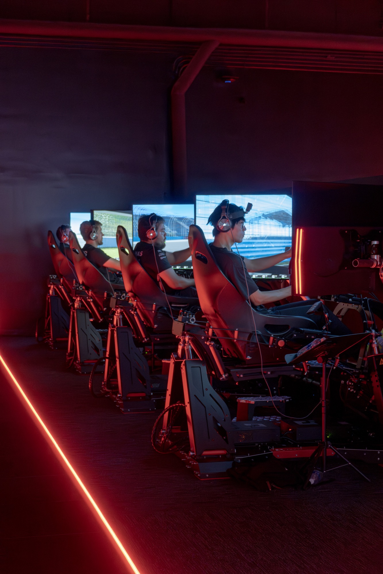 Four drivers racing side by side on a row of World of Racing sims